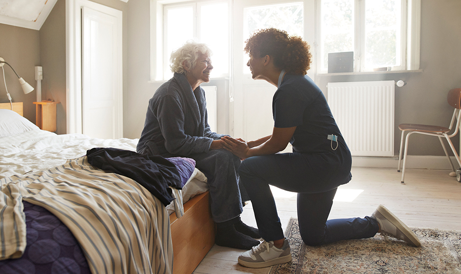 Caregiver kneeling beside a woman sitting on a bed